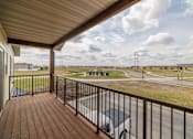 Thumbnail 50 of 76 - A balcony with a wooden floor and a metal railing overlooks a parking lot and a road.