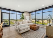 Thumbnail 9 of 61 - A living room with a couch, a chair, and a large window overlooking a balcony.