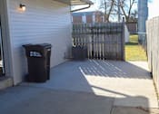 Thumbnail 5 of 18 - A black trash can sits on a concrete patio.
