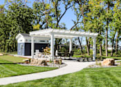 Thumbnail 2 of 15 - A white gazebo is surrounded by a grassy area and trees.