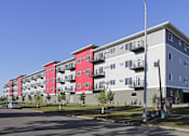 Thumbnail 1 of 19 - A street view of a multi-story building with red and grey sections.