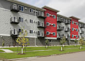 Thumbnail 7 of 19 - Apartment building with red and grey exterior and balconies.