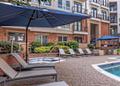 Thumbnail 29 of 58 - A pool area with lounge chairs and umbrellas in front of a brick building.