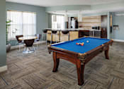 Thumbnail 15 of 36 - A pool table in a room with a bar and kitchen in the background.