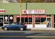 Thumbnail 34 of 36 - A car is parked in front of a pizza shop.