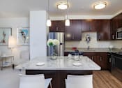 Thumbnail 2 of 36 - A kitchen with a table and chairs in the foreground and a refrigerator, microwave, and oven in the background.