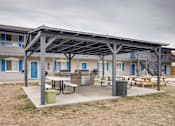 Thumbnail 10 of 12 - A patio area with a table and chairs is covered by a metal roof.