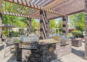 Thumbnail 1 of 20 - Townhomes In Aurora, IL - The Apartments At Kirkland Crossing - Covered Grill Area With Two BBQs, Trees, Counterspace With Bar Chairs.