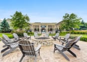 Thumbnail 3 of 15 - Luxury Apartments In Vernon Hills, IL - Outdoor Firepit Lounge Area With Wooden Chairs, and Lush Green Landscaping.