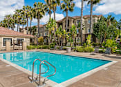 Thumbnail 6 of 30 - A swimming pool surrounded by palm trees and a building in the background.