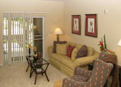 Thumbnail 28 of 30 - A living room with a yellow couch, a chair, and a table with a lamp.