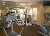 Thumbnail 22 of 30 - A gym with treadmills, elliptical machines, and a television.