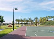 Thumbnail 23 of 30 - A basketball court is surrounded by palm trees and apartment buildings.