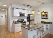 Thumbnail 1 of 18 - One-Bedroom Apartments In Green Lake, Seattle, WA - Circa Green Lake - Kitchen With Hardwood Floor, Stainless Steel Appliances, Kitchen Bar, Pendant Lights, Quartz Countertops, And White Storage Cabinets.