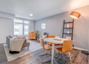 Thumbnail 2 of 18 - Studio Apartments in Green Lake Seattle WA - Circa Green Lake - Living Room with Couch, Area Rug, Dining Area, Wood-Style Flooring, and a Large Window.
