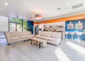 Thumbnail 13 of 18 - Apartments For Rent In Green Lake, Seattle, WA - Circa Green Lake - Resident Clubhouse With Hardwood Floor, Sofas, Kitchen, Counter with Seating Area, And Glass Doors Leading To Courtyard.