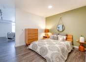 Thumbnail 9 of 18 - Studio Apartments In Green Lake, Seattle, WA - Circa Green Lake - Spacious Bedroom With Hardwood Floor, Bed, Round Mirror, Nightstand with Lamp, Round Side Table, Dresser, and View of Living Room.