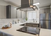 Thumbnail 1 of 31 - Apartments For Rent In Mountain Park, OR - MiLO - Modern Kitchen With Grey Cabinets, Stainless-Steel Appliances, Quartz Countertops, and Window.