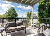Thumbnail 14 of 31 - Mountain Park OR Apartments for Rent - MiLO at Mountain Park - Private Balcony with Patio Furniture and an Area Rug, Surrounded by a View of Trees and the Apartment Building.