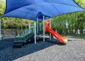 Thumbnail 24 of 33 - Apartments In Coconut Creek for Rent – Waterview at Coconut Creek – playground with a slide and a swing set under a blue umbrella