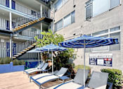Thumbnail 19 of 20 - a patio with lounge chairs and umbrellas in front of an apartment building