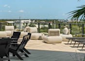 Thumbnail 6 of 18 - A patio with white cushions and black chairs overlooks a cityscape.