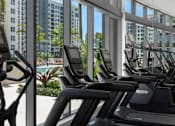 Thumbnail 9 of 18 - A row of treadmills in a gym with a view of a pool and buildings outside the window.