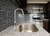 Thumbnail 5 of 15 - A modern kitchen with a stainless steel sink and a brick wall.