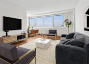 Thumbnail 3 of 59 - A living room with a grey couch, a wooden entertainment center, and a flat screen TV.