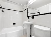 Thumbnail 29 of 59 - A white bathroom with a tub, sink, and toilet.