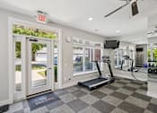 Thumbnail 19 of 26 - A gym with a treadmill, exercise bike, and a television.