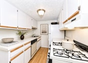 Thumbnail 18 of 21 - Galley kitchen with white cabinets and gas stove at Stonetree Apartments, East Point, GA