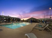 Thumbnail 24 of 36 - A pool area with sun loungers and a building in the background at dusk.