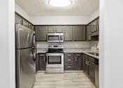 Thumbnail 7 of 26 - A kitchen with a stainless steel refrigerator, microwave, oven, and cabinets.