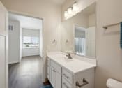 Thumbnail 25 of 56 - A bright bathroom with a white vanity, large mirror, and modern light fixtures. The room features a towel bar and a glimpse of the adjacent room visible through the door.