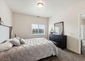 Thumbnail 23 of 56 - A cozy bedroom with a bed, decorative pillows, a dresser, and a mirror. The room features a window with natural light and leads into another space through an open door.