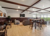 Thumbnail 47 of 56 - A spacious community room with modern seating arrangements, including high-top tables with chairs and lounge areas with sofas. Large windows offer a scenic view, and a flat-screen TV is mounted on the wall. The room has a bright, inviting atmosphere.