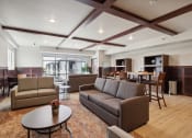 Thumbnail 46 of 56 - A stylish community lounge with comfortable seating, including sofas and armchairs, a coffee table, and high-top tables with chairs. The space has modern decor, wood accents, and large windows letting in natural light.