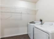 Thumbnail 27 of 56 - A laundry room featuring a washer and dryer, with wire shelving above for storage. The space has wood-style flooring and a simple, clean design.