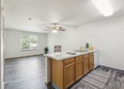 Thumbnail 5 of 31 - Open-concept apartment kitchen and living area featuring wood cabinetry, a white countertop, and a dishwasher. The space has wood-style flooring, a ceiling fan with a light fixture, and a large window providing natural light