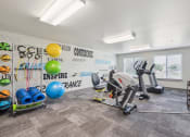 Thumbnail 20 of 31 - Apartment community fitness center featuring a recumbent bike, two treadmills, and a variety of workout equipment, including resistance bands, stability balls, and foam rollers. The well-lit space has large windows, carpeted flooring, and a wall-mounted TV for entertainment