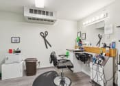 Thumbnail 26 of 31 - Community hair salon featuring a black styling chair, a wash station with a sink, and a well-lit vanity mirror. The space includes salon tools, hair care products, and decorative elements such as wall-mounted scissors, creating a functional and inviting setting