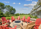 Thumbnail 57 of 58 - a patio with red chairs and a fire pit and an apartment building