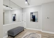 Thumbnail 4 of 26 - A room with a bench, a mirror, and a painting on the wall.