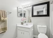 Thumbnail 17 of 28 - A white bathroom with a toilet, sink, and mirror.