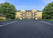 Thumbnail 5 of 25 - A large yellow building with a parking lot in front.