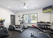 Thumbnail 7 of 14 - A gym with a row of treadmills, a stationary bike, a rowing machine, and a television showing a baseball game.