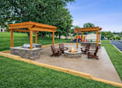 Thumbnail 3 of 13 - A patio with a fire pit and chairs under a wooden pergola.