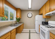 Thumbnail 8 of 21 - A kitchen with a white refrigerator, a white stove, and a clock on the wall.