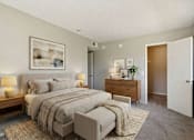 Thumbnail 19 of 21 - A bedroom with a large bed, a nightstand with a lamp, and a dresser with a plant on top.